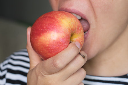 Close-up of a person biting into a fresh apple, highlighting the crisp texture and juiciness. Concept: Emphasizing the health benefits and enjoyment of eating fresh, natural fruits.の写真素材