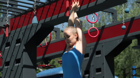 In a blue athletic outfit, a woman performs a stretch at an outdoor gym, her eyes closed in peaceful...