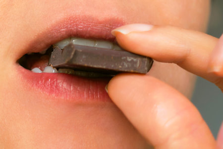 close-up of a person biting into a piece of dark chocolate, highlighting the rich flavor and indulgence of the treat. This image conveys a moment of sensory pleasure, perfect for gourmet, snack, or food-related concepts.の写真素材