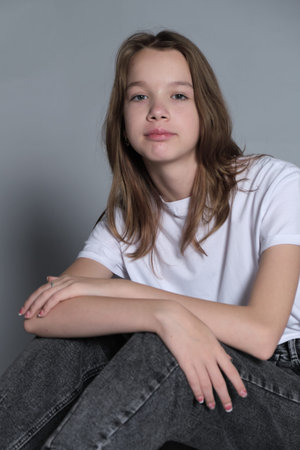 A girl sits comfortably on the floor, casually resting her hand on her head. The neutral background...