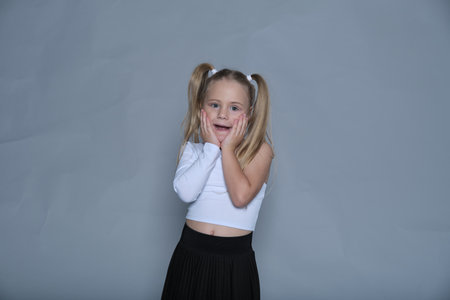 little girl shows off her bold and joyful personality with a playful pose, making the most of the studio setting. Her trendy one-shoulder top and pleated skirt add a stylish flair to the energetic moment.の写真素材