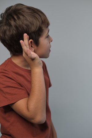 boy attentively listens, hand to ear, a gesture of focus. This image reflects the importance of listening in learning environments amid digital distractions.の写真素材