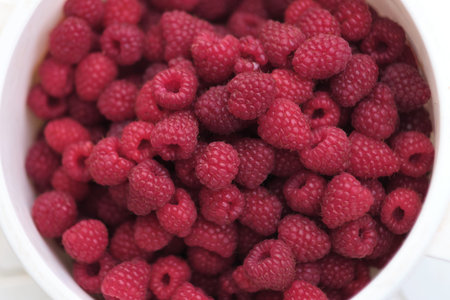 close-up of freshly picked ripe raspberries in a white bowl. vibrant red berries create a visually...