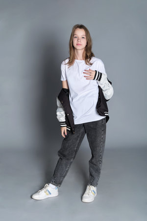 A young girl casually holds her jacket and looks down thoughtfully. This image reflects a moment of...