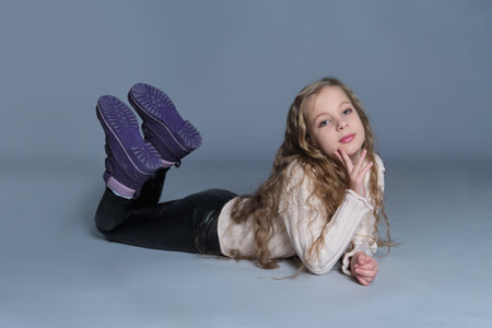 A girl makes peace signs with her hands while lying down, dressed warmly in a sweater and boots. This portrait radiates a sense of fun and relaxation, ideal for themes of youthful happiness and cozy style.の写真素材