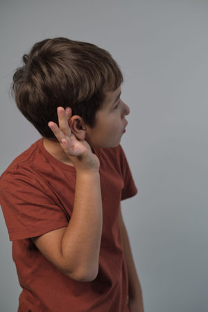 boy attentively listens, hand to ear, a gesture of focus. This image reflects the importance of listening in learning environments amid digital distractions.の写真素材