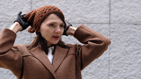 A stylish woman wearing gloves fixes her warm hat, blending fashion with practicality.