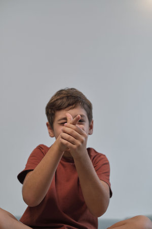 A playful boy sitting cross-legged on a sofa, pretending to aim with his hands. His joyful demeanor...