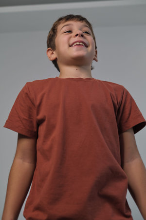 A smiling boy is captured from a low angle, emphasizing his cheerful expression and confident...