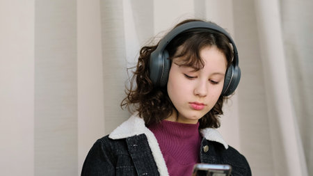 A contemplative young girl listens to audio through her headphones, her eyes focused beyond the frame. This image reflects a moment of peace and self-reflection.の写真素材