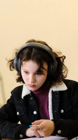 A thoughtful girl balances her focus between writing and technology at her desk. The scene captures themes of productivity, adaptability, and the modern approach to education.の写真素材