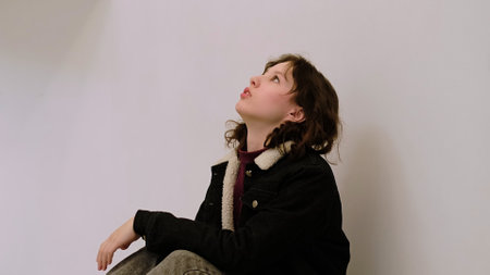 A pensive girl leans forward with her hand on her forehead, deep in thought.の写真素材