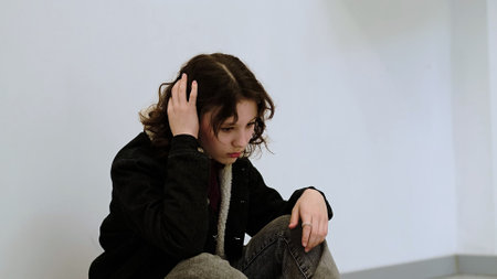 A girl sits cross-legged on the floor, her expression contemplative and subdued. This photo highlights the quiet moments of self-reflection and the complexity of youth emotions.の写真素材