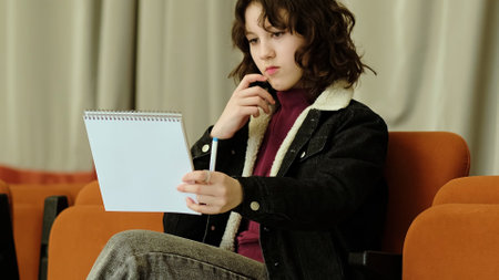 A young girl holds a notebook and pen with a determined expression. This image conveys themes of focus, creativity, and youthful energy in a casual setting.の写真素材