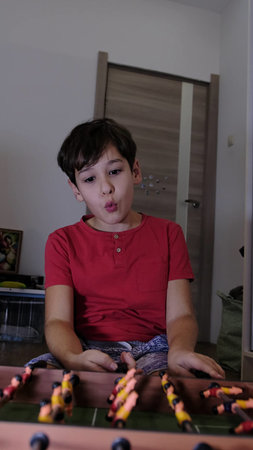 A boy in a red shirt is playing table football with vivid emotions, expressing excitement and joy. The scene conveys dynamics and lively energy.の写真素材