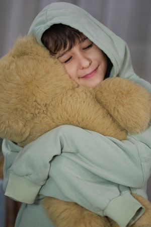 A young boy in a hooded sweater, embracing a soft teddy bear with a peaceful expression.の写真素材