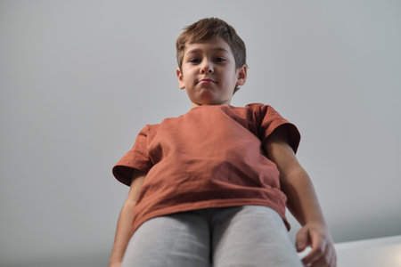 A confident boy stands tall, captured from a low-angle perspective, giving a sense of strength and curiosity. This image highlights individuality and youthful energy.の写真素材