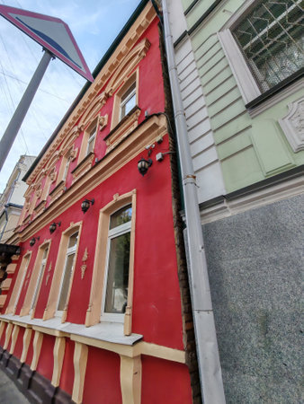 Close-up of a red exterior wall with decorative beige accents, a detailed iron canopy, and lush potted plants. The vivid colors contrast beautifully, highlighting traditional architecture in a modern setting.の写真素材