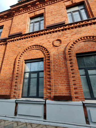 Detailed shot of an old red brick facade featuring arches and framed windows. The historic design emphasizes durability, symmetry, and urban aesthetic.の写真素材