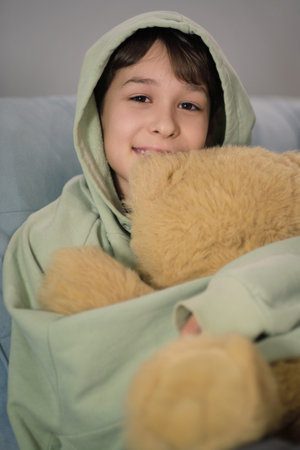 The boy embraces a soft teddy bear, evoking themes of childhood innocence and emotional connection.の写真素材