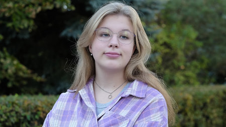 A young woman with glasses and a plaid shirt smiles softly, gazing away in a peaceful outdoor setting. This photo captures natural beauty and a serene moment of reflection.の写真素材
