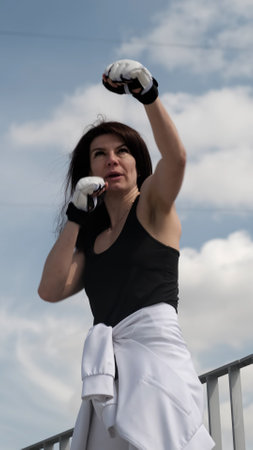 A determined woman throws a punch towards the sky, her expression filled with focus and strength. The rise of female empowerment in sports highlights resilience, confidence, and mental toughness.の写真素材