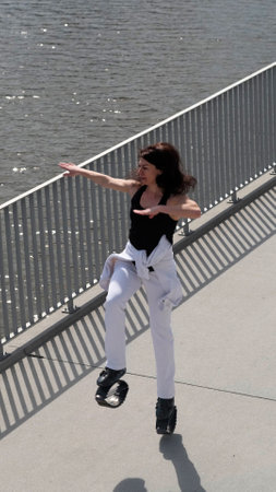A woman in Kangoo Jumps boots moves energetically along a waterfront promenade, enjoying the outdoor workout. The rise of innovative fitness gear reflects the growing trend of fun and engaging physical activities.の写真素材