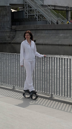A woman in white sportswear stands near a railing by the water, wearing Kangoo Jumps rebound shoes. The fusion of urban fitness and scenic surroundings highlights the modern trend of outdoor workouts.の写真素材