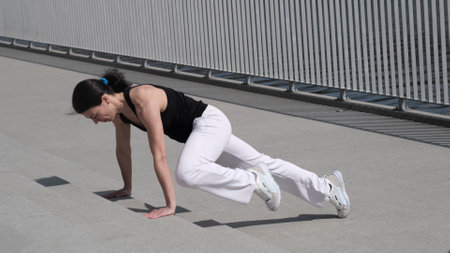 A fit woman engages in a high-intensity workout, executing mountain climbers with precision. The urban setting adds a sense of determination and discipline to the scene.の写真素材