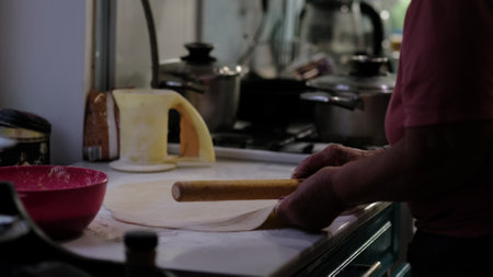 An experienced cook rolls out dough, creating a dish from scratch in a warmly lit kitchen. The image emphasizes the authenticity of homemade food and the dedication behind preparing meals with care.の写真素材