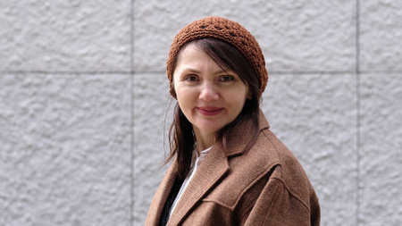 A woman in a knitted hat and warm coat gazes at the camera with a kind and genuine smile.の写真素材