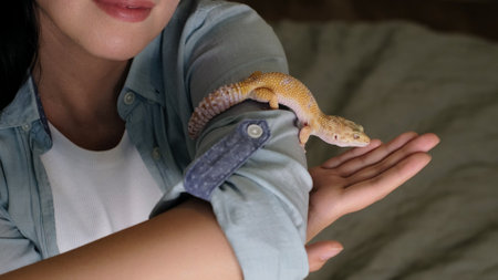 A close-up of a smiling woman interacting with a gecko on her arm. The image emphasizes companionship and the growing appreciation for reptiles as calming pets.の写真素材