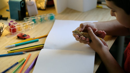 A child holds a leopard gecko while surrounded by colorful pencils and a blank sketchbook on a desk. This photo reflects creativity, curiosity, and a bond with exotic pets.の写真素材
