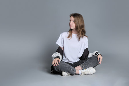 A girl in a casual outfit sits cross-legged, lost in thought. This image highlights the blend of innocence and emerging maturity, symbolizing the journey of self-discovery and individuality.の写真素材