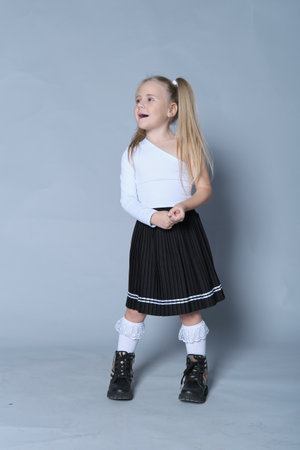 A stylish young girl is dressed in a fashionable school uniform-inspired outfit, featuring a black pleated skirt, lace socks, and boots. Her cheerful pose and polished look make this photo perfect for back-to-school promotions or educational campaigns.の写真素材