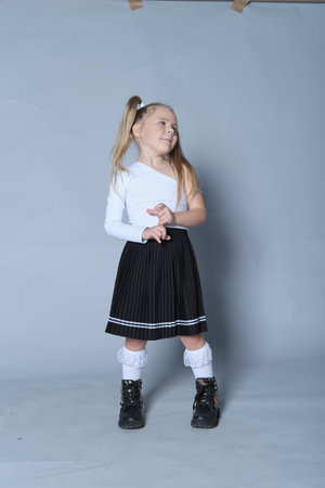 playful and confident little girl poses with her hand on her hip and a smile on her face. Dressed in a trendy one-shoulder top and black skirt, her personality shines through in this lively portrait, ideal for themes of childhood joy and self-expression.の写真素材
