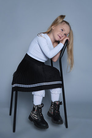 fun moment from a childrens fashion shoot, where a 5-year-old girl, dressed in a trendy outfit, sits playfully on a chair. Her bright laughter and energetic pose make this image perfect for kids fashion or lifestyle campaigns.の写真素材