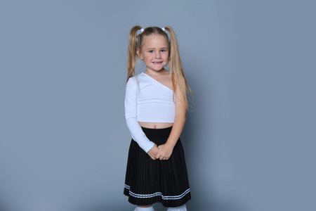 Wearing a white one-shoulder top and a black pleated skirt, a young girl with blonde pigtails grins mischievously. This image captures her playful energy and the innocence of childhood.の写真素材