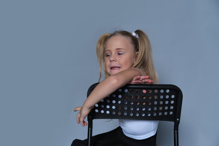 fun moment from a childrens fashion shoot, where a 5-year-old girl, dressed in a trendy outfit, sits playfully on a chair. Her bright laughter and energetic pose make this image perfect for kids fashion or lifestyle campaigns.の写真素材