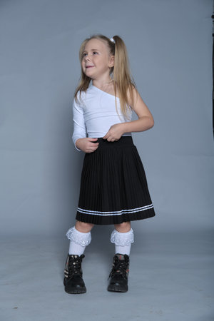 Dressed in a chic outfit, a 5-year-old girl smiles slightly, showing her playful yet poised side during a modeling shoot.の写真素材