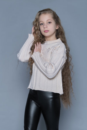 A girl with wavy hair smiles and makes a playful gesture, dressed in a cozy sweater. This scene highlights a carefree attitude, combining childrens fashion with natural hair care themes.の写真素材
