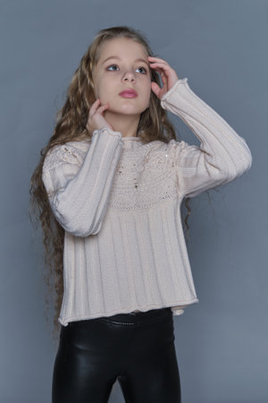 A girl in a light sweater gently touches her face, showing off her long, wavy hair and a calm expression. The scene underscores the importance of caring for childrens hair, while also promoting comfort and style in kids fashion.の写真素材