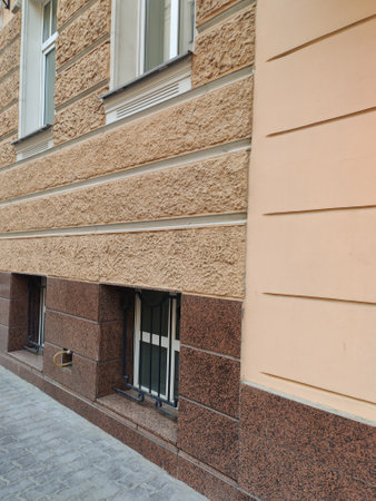 Close-up of a peach-colored building featuring intricate stone textures, decorative window moldings, and a mounted security camera. The photo highlights the contrast between old-world charm and modern security systems.の写真素材