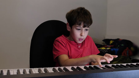 The boy sits at the piano keyboard, engaged in learning a new melody, embodying focus and determination.の写真素材