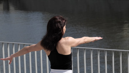 A fit woman exercises outdoors, extending her arms against the backdrop of the water. The image reflects freedom, balance, and inner strength.の写真素材
