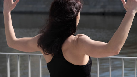 A woman with athletic shoulders and arms exercises outdoors, emphasizing physical strength. The...