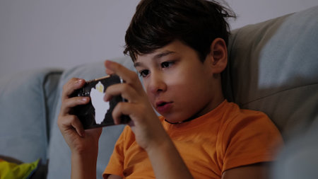 young boy is fully immersed in a smartphone game, his face lighting up with excitement. The scene captures the entertainment and wonder of digital play for kids.の写真素材