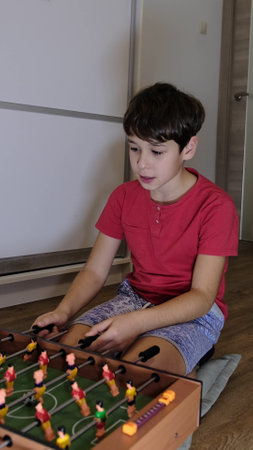 A boy in a red shirt smiles while playing foosball, enjoying a fun and competitive moment at home.の写真素材