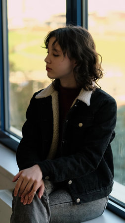 A girl seated by a window with sunlight streaming in reflects a peaceful, introspective moment. This image explores themes of mindfulness, simplicity, and quiet self-reflection.の写真素材