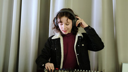 A girl adjusts a sound mixer while singing, her headphones emphasizing the focus on audio. The photo captures the joy of engaging in creative and musical tasks.の写真素材